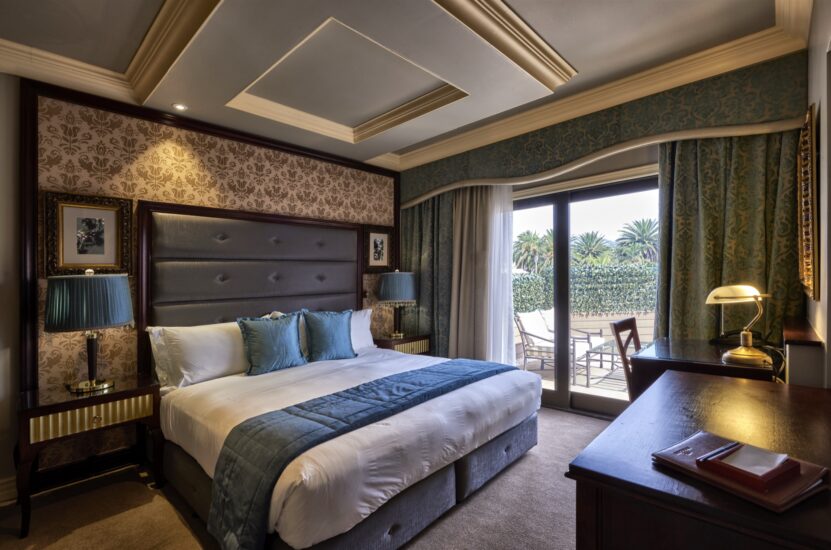 Deluxe room with king bed, teal accents and garden-view patio doors at the D'oreale Grande, Emperors Palace