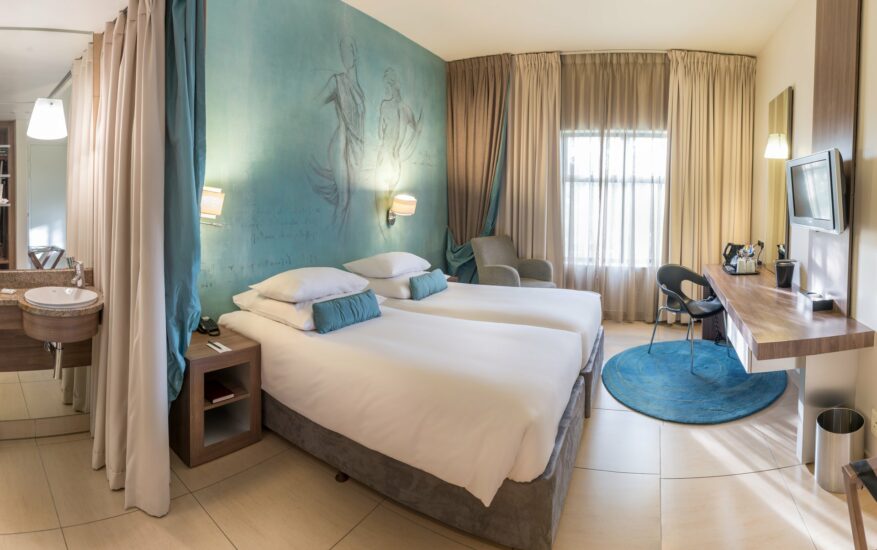 Classic Twin Room with joined beds, teal mural wall, armchair and work desk at Metcourt, Emperors Palace