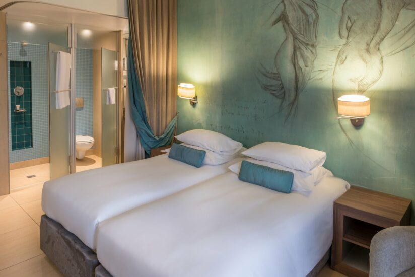 Classic Twin Room with teal bolster cushions and a glass shower at Metcourt, Emperors Palace