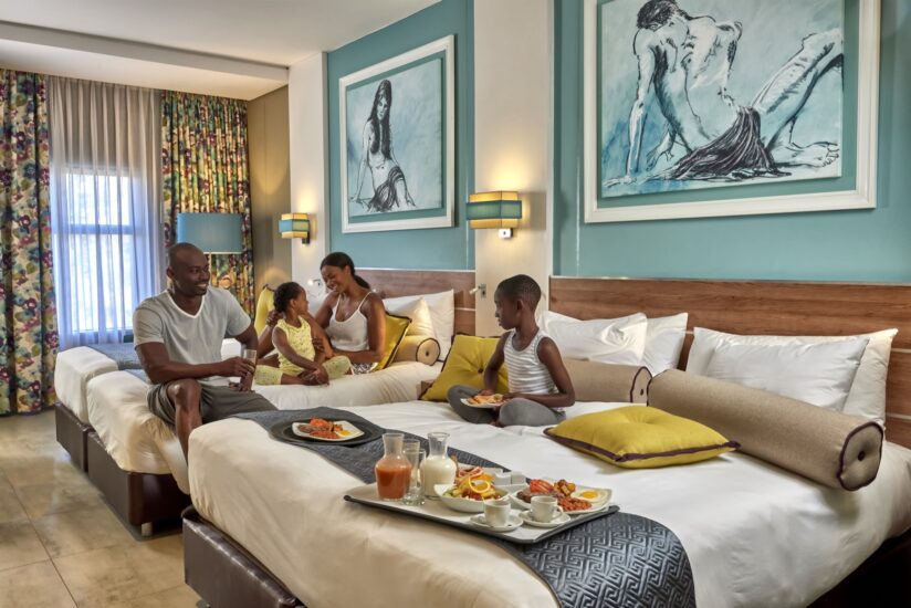 A family enjoys breakfast in bed across twin beds in a Family Room at Metcourt, Emperors Palace