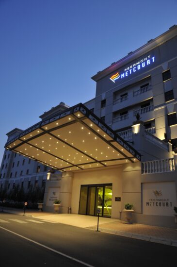 The illuminated Peermont Metcourt hotel entrance canopy glows at twilight at Emperors Palace