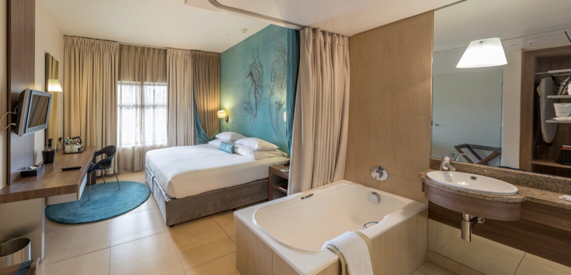 A Superior Room with double bed, work desk, wall-mounted TV and open bathtub at Metcourt, Emperors Palace