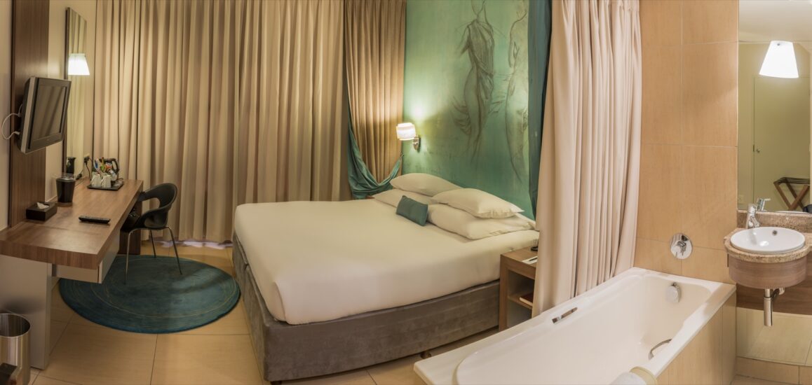 A Superior Room showing a green wall mural, bathtub and basin beside the double bed at Metcourt, Emperors Palace
