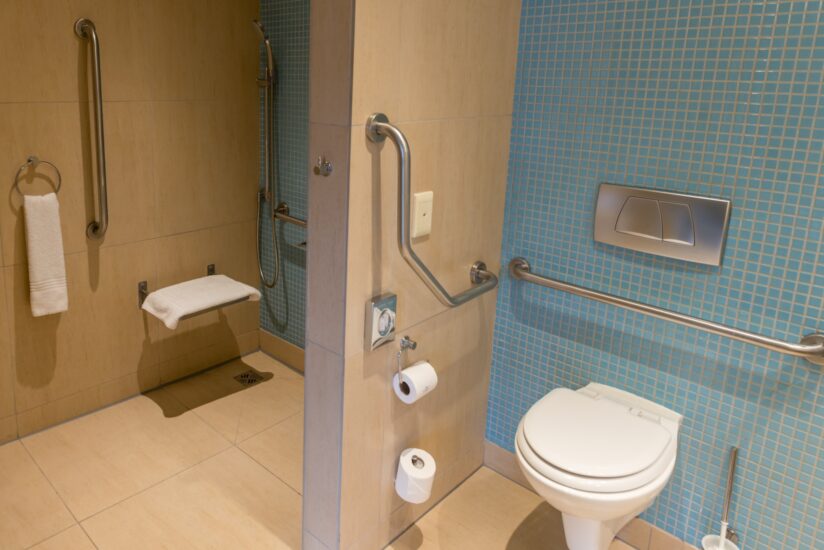 An accessible bathroom with grab rails, a fold-down shower seat and wall-hung toilet at Metcourt, Emperors Palace