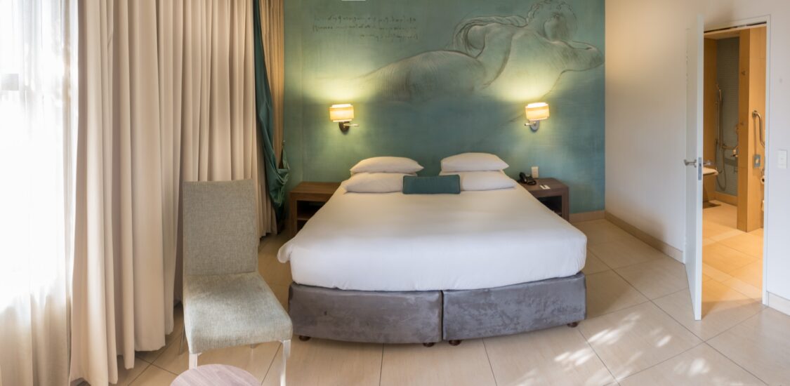 A daylit accessible room with a reclining-figure mural and open accessible bathroom at Metcourt, Emperors Palace