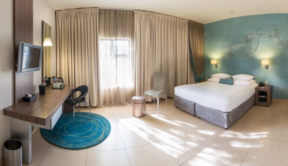 A spacious accessible room with wide floor space, desk, TV and mermaid mural at Metcourt, Emperors Palace